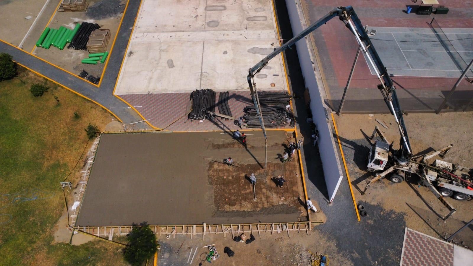 Vista aérea de una losa de cancha a medio vaciar, con operarios extendiendo el concreto y un camión bomba al lado