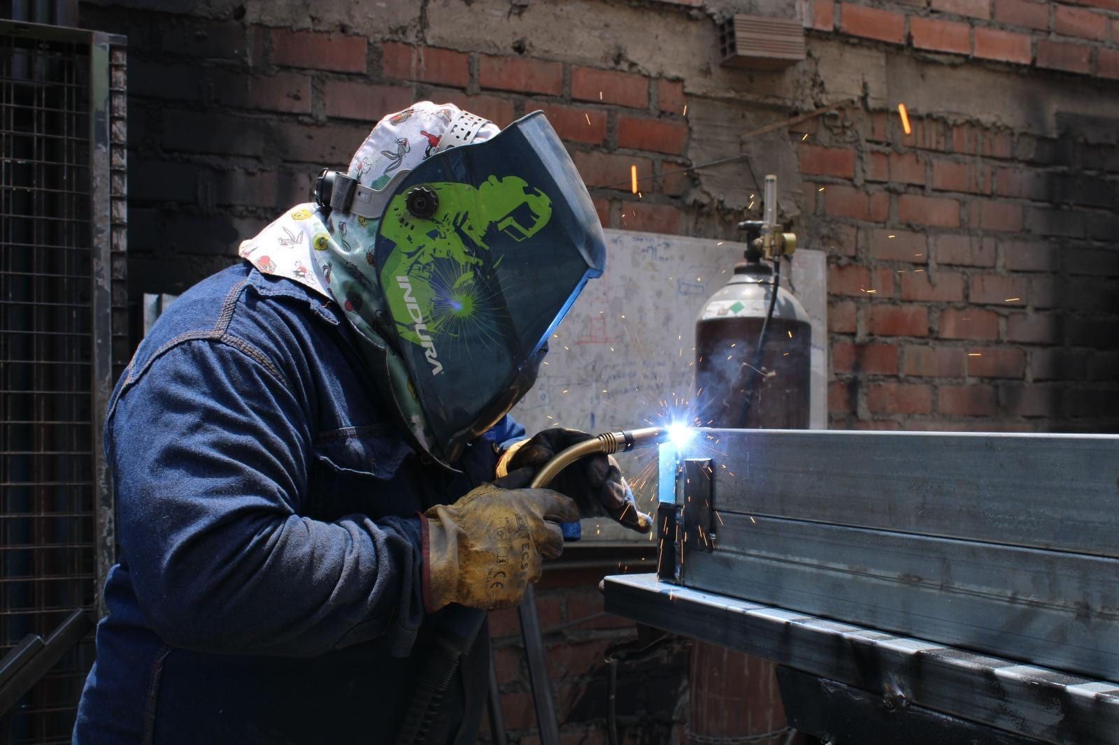 Soldador con careta y guantes soldando un perfil de acero en el taller